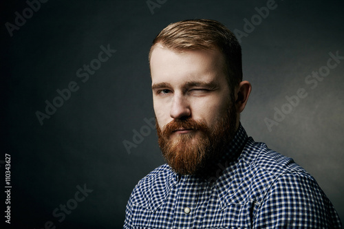Winking red bearded man studio portrait on dark background