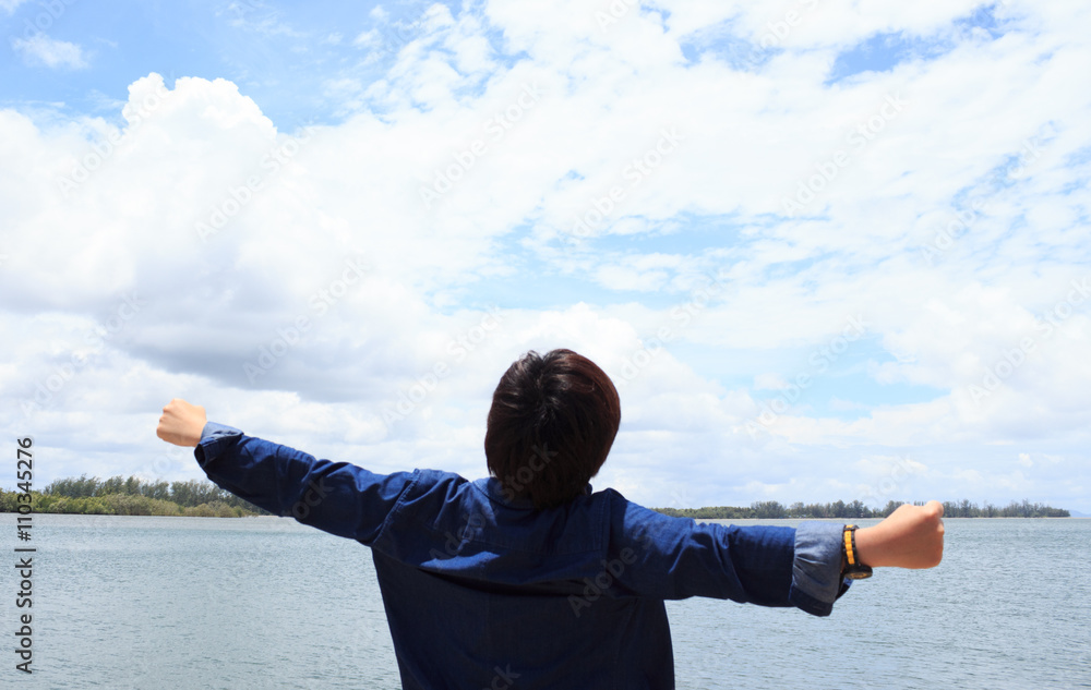 back of young man wear shirt jeans and arms wide open in front of sea back of young man wear shirt jeans and arms wide open in front of sea