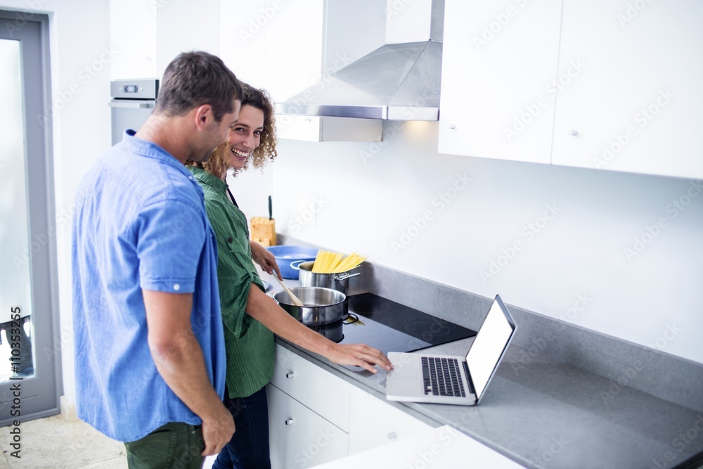 Obraz premium Couple working on laptop while cooking