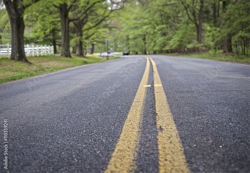 DOUBLE YELLOW LINE ON ASPHALT ROAD, USA (THE IMAGE HAS SHALLOW DEPTH OF FIELD, FOCUS AT IMMEDIATE FOREGROUND) 