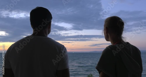 Man and woman standing and looking at sea in the dusk. There is a distance expressing disunity and chill in their relationships photo