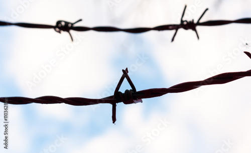 Barbed wire silhouetted against a cloudy blue sky