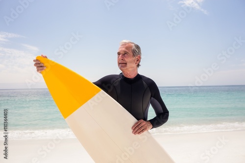 Happy senior man in wetsuit holding a surfboard