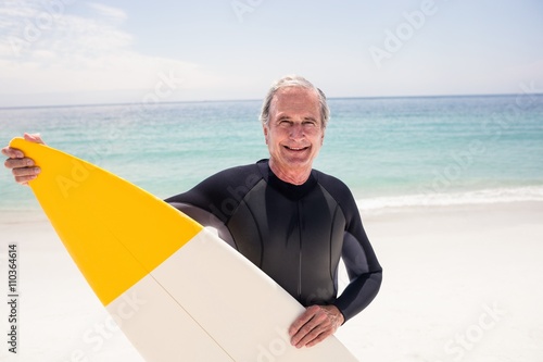 Portrait of senior man in wetsuit holding a surfboard
