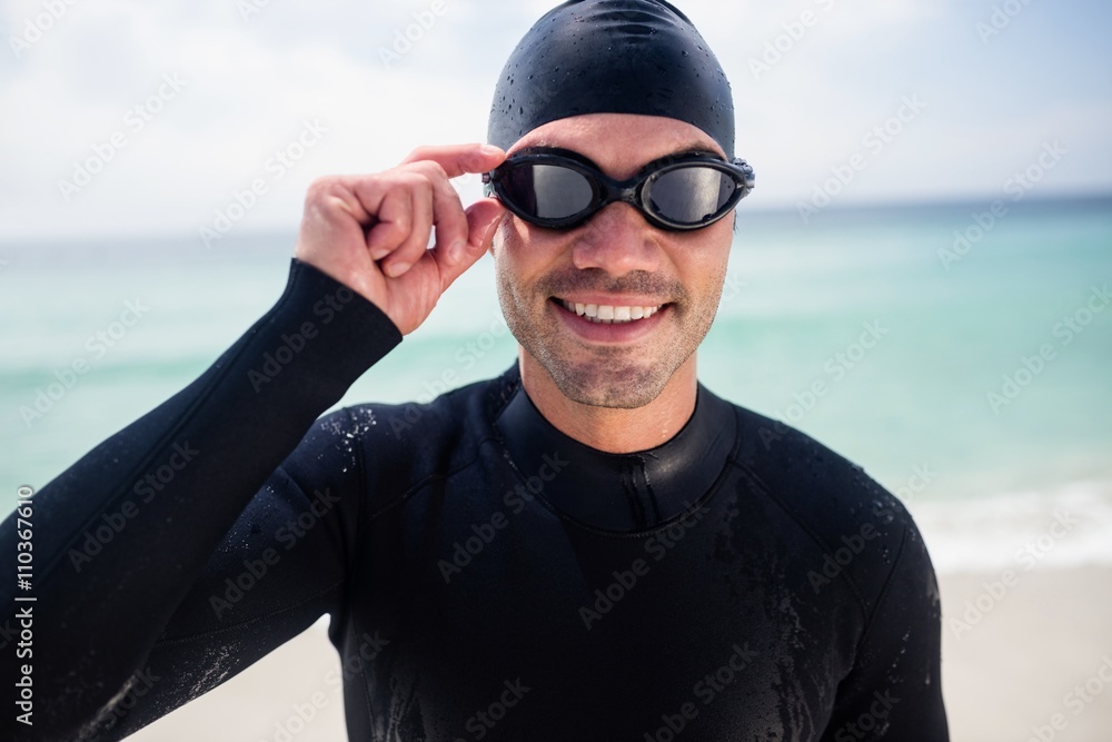 Young man in wetsuit and swimming goggles standing on beach Young man in wetsuit and swimming goggles standing on beach
