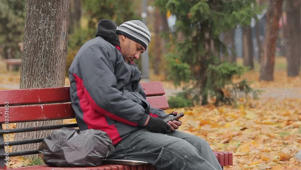 Male alcohol addict having a nap on bench in autumn park with bottle in hand Male alcohol addict having a nap on bench in autumn park with bottle in hand