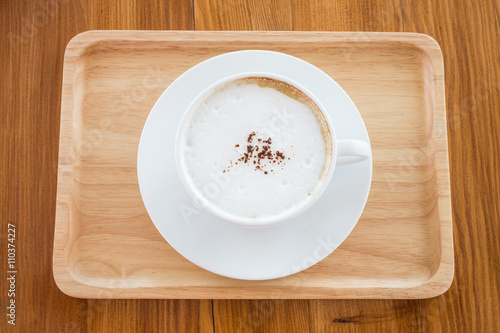 cappuccino in a white cup on a wooden plate on table