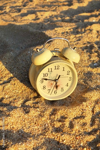 Vintage clock on sand with sunlight