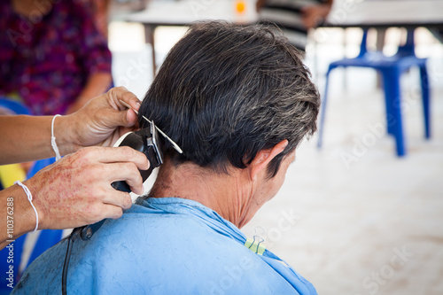 Old man having a haircut with a hair clippers in barber shop