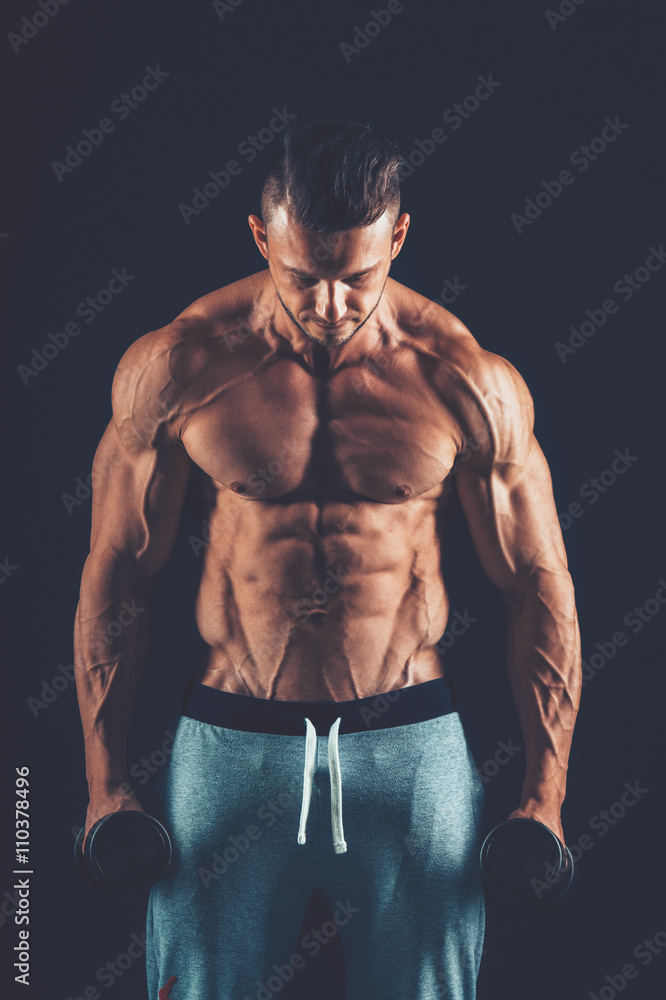 Fototapeta premium Closeup of a muscular young man lifting dumbbells weights on dar