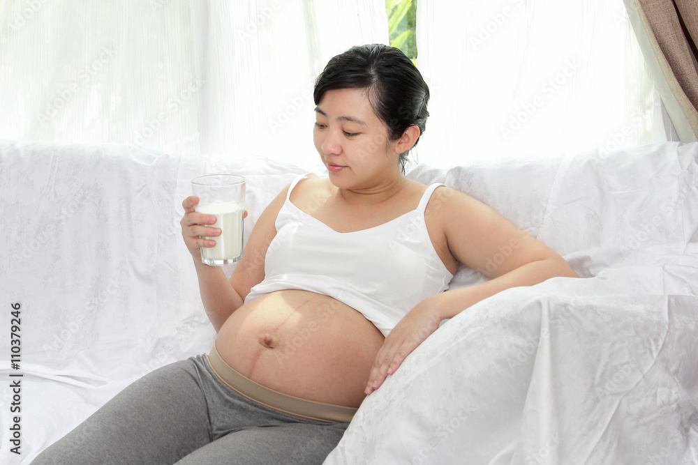 Beautiful asian woman pregnant holding glass of milk in the home with lighting of sunlight Beautiful asian woman pregnant holding glass of milk in the home with lighting of sunlight