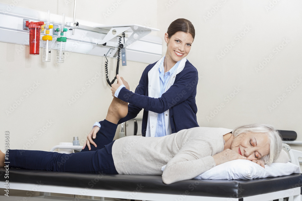 Obraz premium Happy Physiotherapist Helping Senior Woman With Leg Exercise