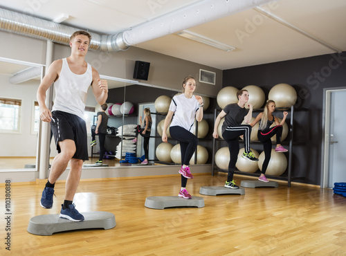 Men And Women Performing Step Exercise In Gym