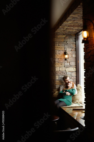 Hugging couple sitting on window-sill