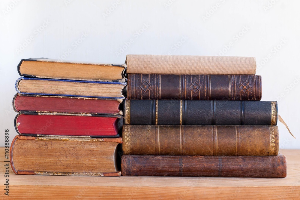 Stack of old books lying on wooden shelf  