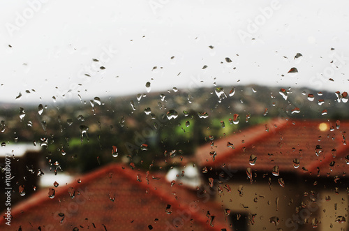glass with rain drops on background of houses red roofs