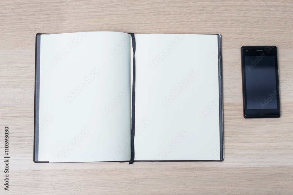 Open notebook with phone on wooden table, top view Open notebook with phone on wooden table, top view