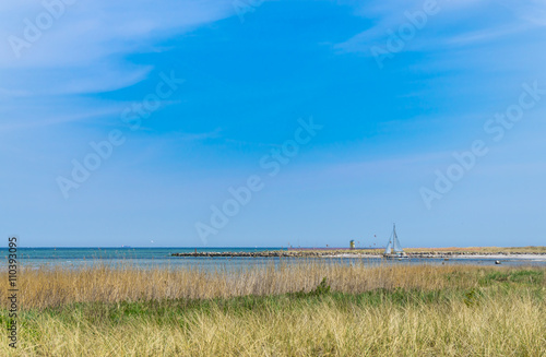 Ein Segelboot verlässt den kleinen Hafen von Marina Wendtorf - im Vordergrund sieht man die Dünen und im Hintergrund die Ostsee