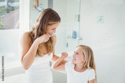 Smiling mother and daughter brushing teeth