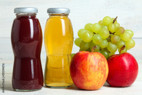 glass bottles of juice and an Apple with grapes on a white wooden background