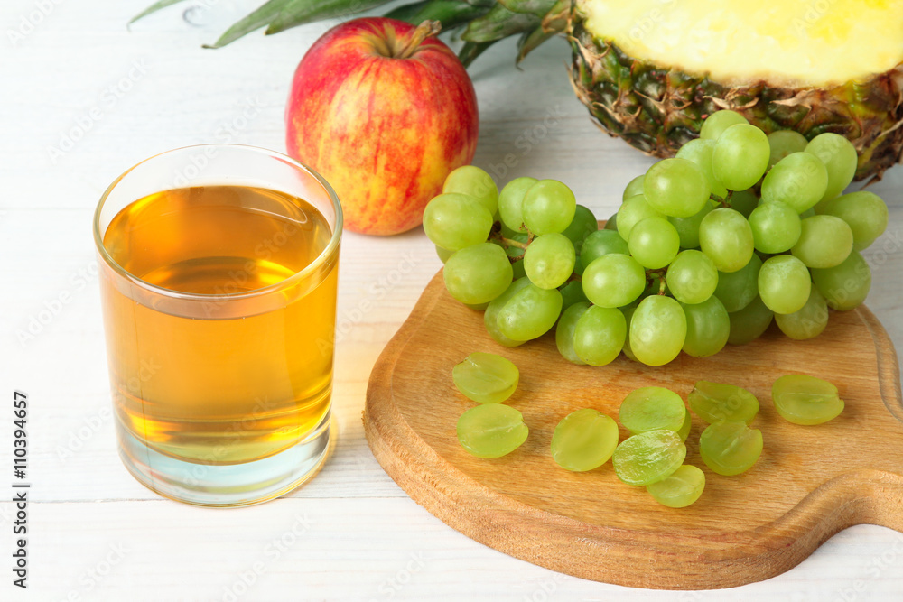 grape juice in a glass on a cutting Board with a bunch of grapes and apple with pineapple on white wooden table grape juice in a glass on a cutting Board with a bunch of grapes and apple with pineapple on white wooden table