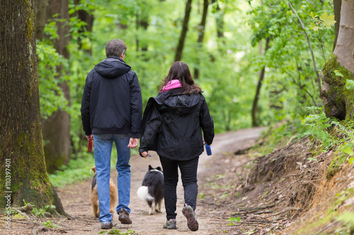 Photography Middle aged couple walking their two dogs in forest.