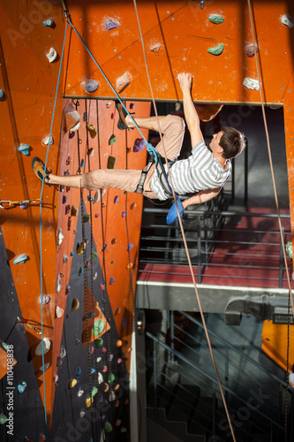 Athletic man with special equipment climbs on an indoor rock-climbing wall. Holding one hand in bag with powder chalk magnesium