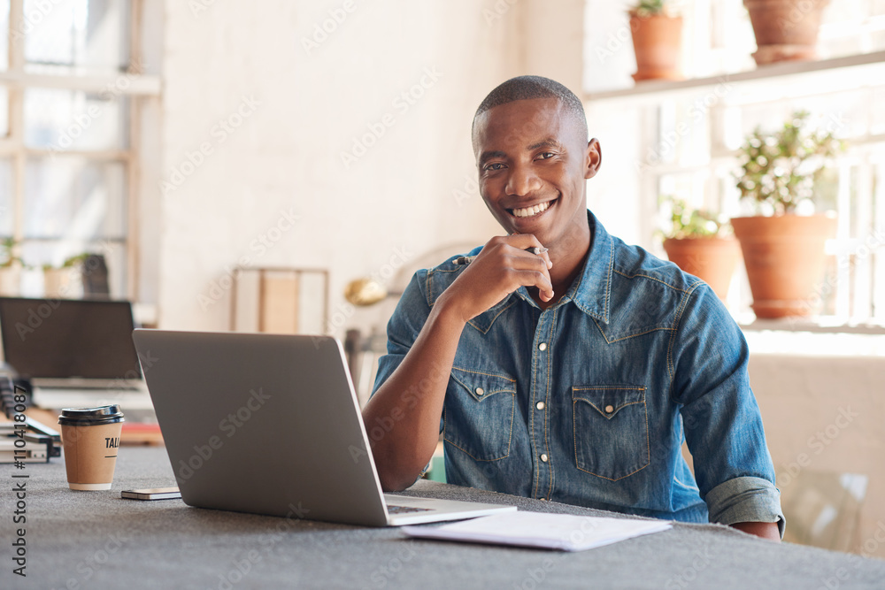 Smiling African designer with laptop in beautifully lit studio