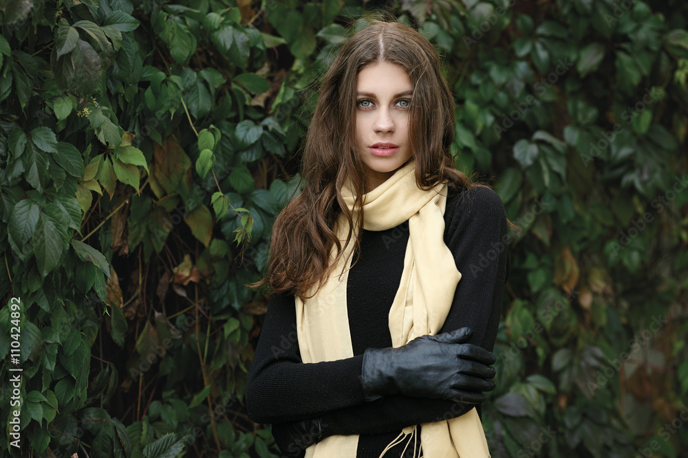 Outdoor portrait of young beautiful brunette woman with wavy long hair hugging herself posing against ivy wall background Outdoor portrait of young beautiful brunette woman with wavy long hair hugging herself posing against ivy wall background
