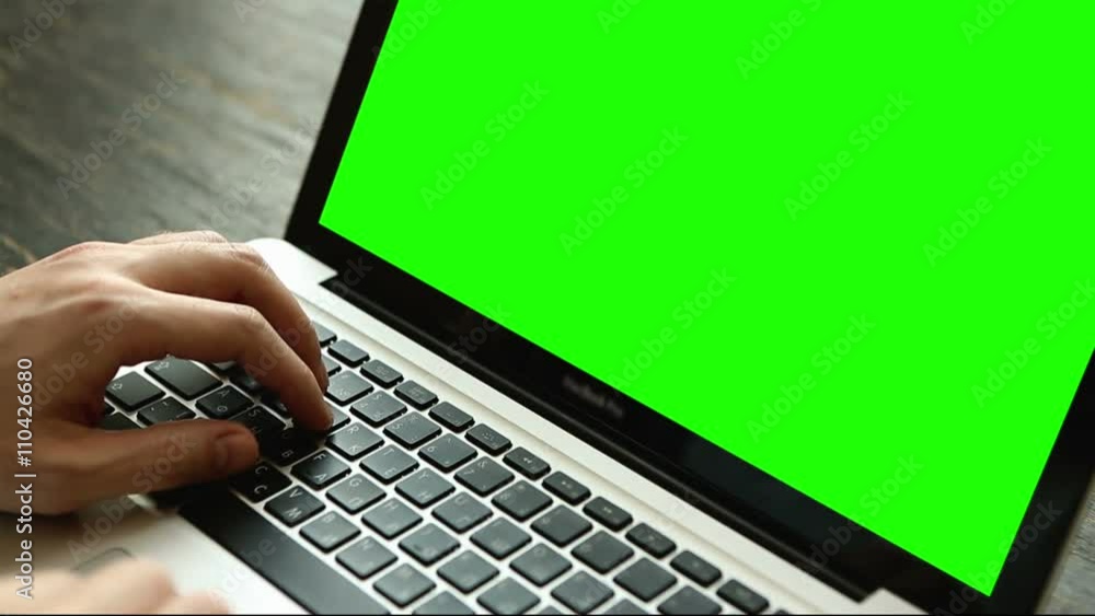 Hand of a man working at laptop computer typing on a keyboard on dark desktop. Close up view with green screen Hand of a man working at laptop computer typing on a keyboard on dark desktop. Close up view with green screen