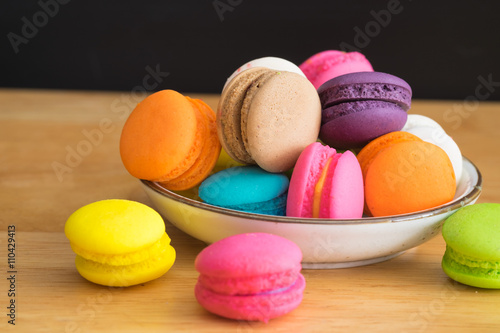 colorful macaroon in white ceramic plate with all flavors on wooden table/colorful macaroon in ceramic plate