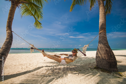 young woman smiling and relaxing in a hammock by the beach