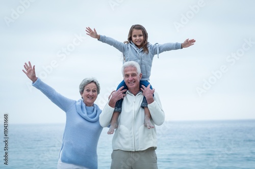 Grandparents and granddaughter with arms outstretched at beach