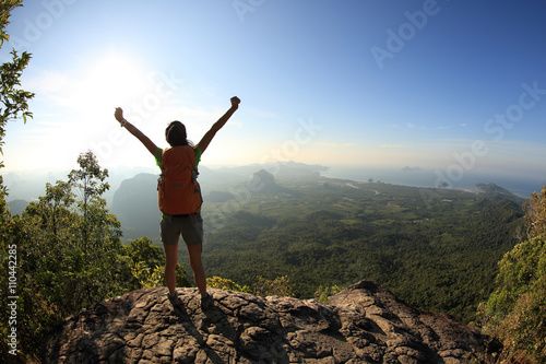 silhouette of young successful woman hiker open arms on mountain peak