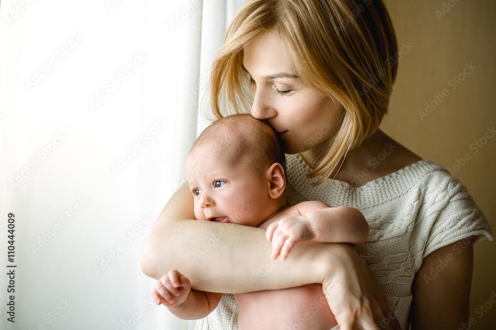 newborn baby in a tender embrace of mother at the window