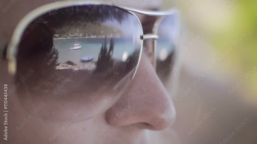 Beach with white boar reflected in brown mirrored sunglasses, close up of woman face Beach with white boar reflected in brown mirrored sunglasses, close up of woman face