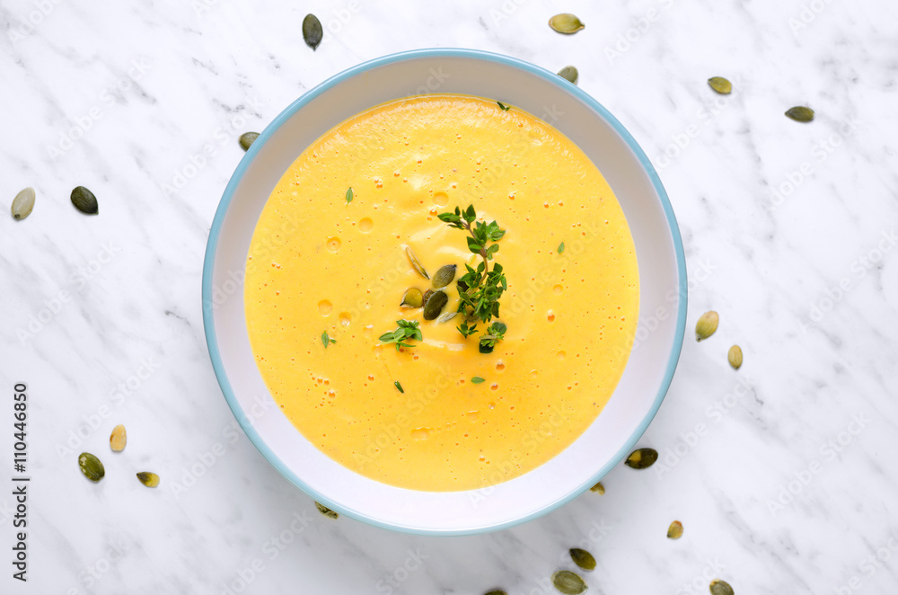 Pumpkin soup in a bowl with spoon on a marble and thyme