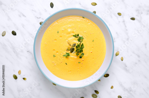 Pumpkin soup in a bowl with spoon on a marble and thyme