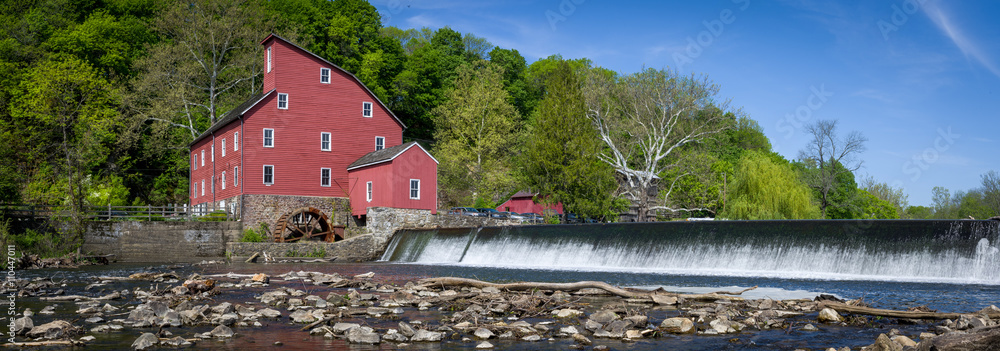 Naklejka premium Panoramic view of historic red mill building on river with dam