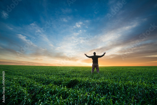happy young man on green field of wheat at sunrise