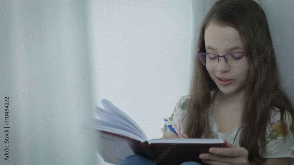 Emotional little girl with glasses writes in his diary at window. Emotional little girl with glasses writes in his diary at window.