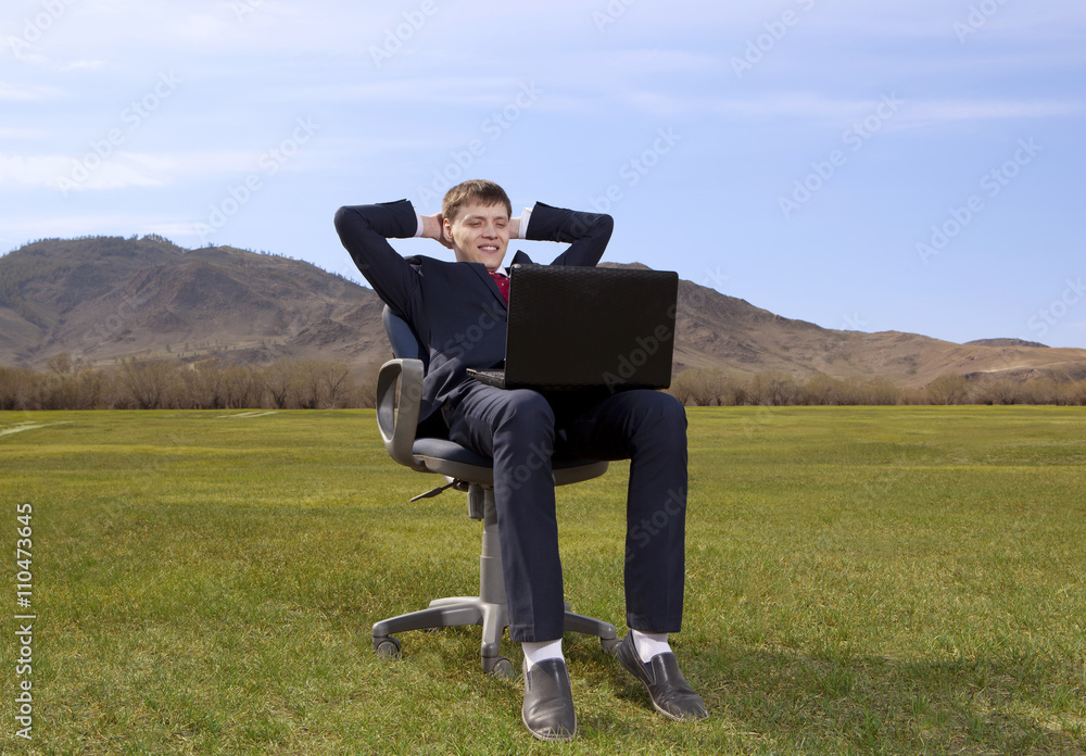 Businessman sitting on chair with a laptop on green meadow Businessman sitting on chair with a laptop on green meadow