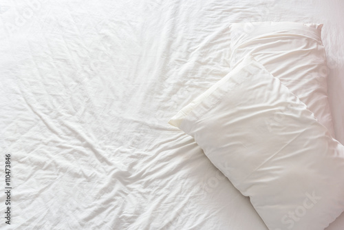 Top view of an untidy / unmade bed with white crumpled bed sheet and two messy pillows in a hotel room. An accommodations that is not neatly arranged for a new guest / customer / visitor to sleep in.