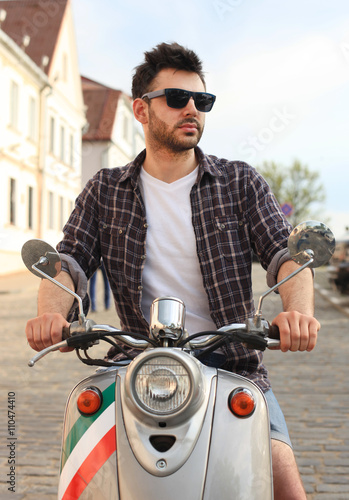 fashionable young man riding a vintage scooter in the street