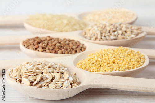 various cereals in wooden spoons on a white wooden table closeup