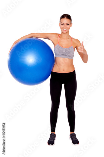 She's ready for a full body workout! Portrait of an attractive and sporty young woman holding a pilates ball and thumb up to camera while stranding isolated.