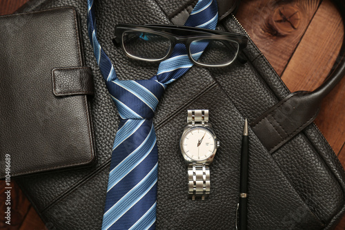 Business man essentials: leather wallet, blue tie, watch and pen.