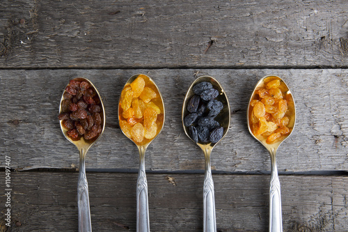 Raisins in metal spoons on wooden table