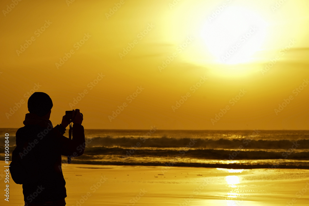 young man taking a picture in front of the sea at dusk
