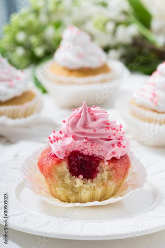 Cupcake with berry jam and pink cream on a white plate, vanilla cupcakes with white creamon the background, close up, selective focus